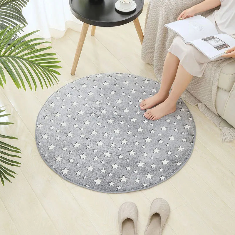 Round grey kids rug with white star print placed on a light wood floor beside a sofa