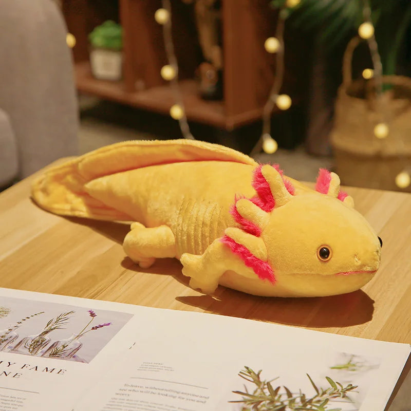 Yellow plush axolotl toy on a wooden surface with a magazine underneath