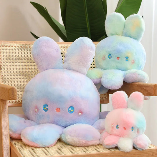 Pastel-coloured plush toys with bunny ears on a wooden chair.