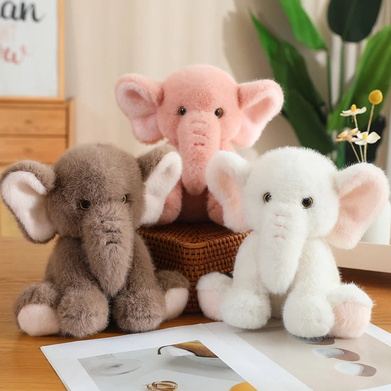 A pink, white and brown soft plush elephant toys sat on a hard surface.