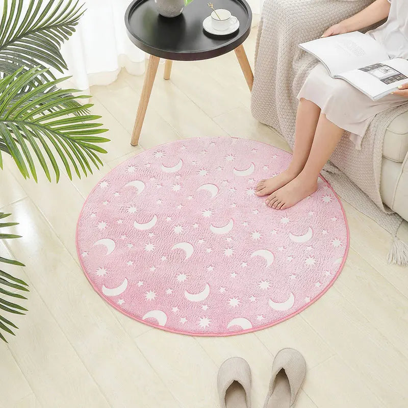 Round pink rug with moon and star pattern on a light wooden floor.