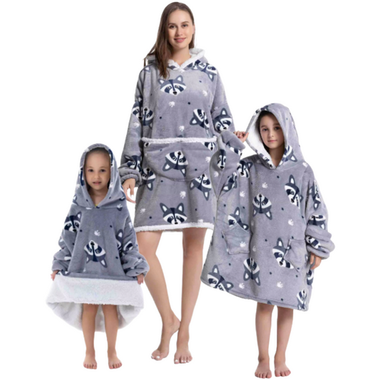 Adult and children wearing grey oversized wearable hoodies featuring a playful raccoon print and soft sherpa lining