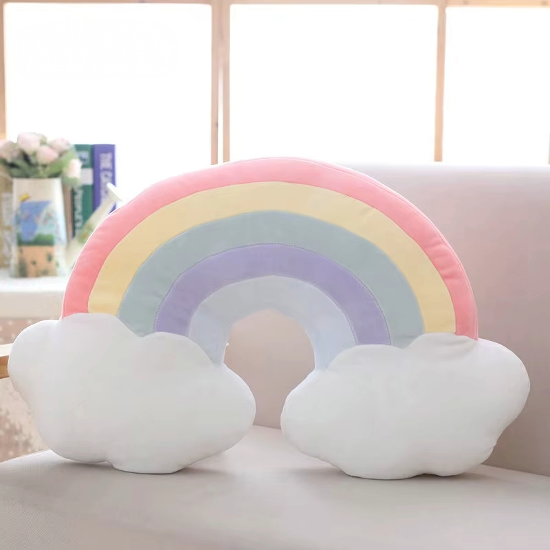 Pastel rainbow plush pillow with soft cloud details displayed on a sofa